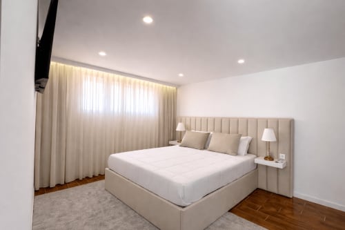 Quarto deluxo moderno em Quinta das Susandas com cama king, cabeceira bege, cortinas creme, pisos de madeira e iluminação