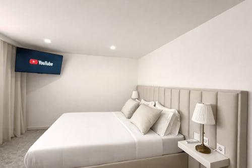 Quarto moderno da Quinta das Susandas com cama, TV, luminária na criada-muda e janela com vista para piscina no hotel português