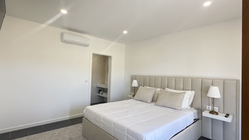 Quarto de luxo moderno na Quinta das Susandas com cama queen, cabeceira bege, banheiro privativo, ar-condicionado e decoração neutra.