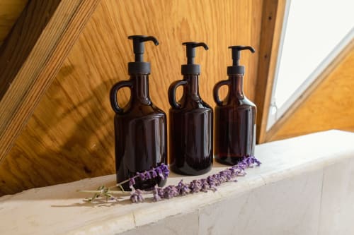 Tres botellas dispensadoras de vidrio oscuro con flores secas púrpura, amenidades de lujo en Meraki Glampings, Malinalco