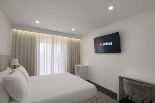 Quarto deluxo moderno na Quinta das Susandas com cama branca, TV de parede, cortinas translúcidas e acesso à varanda