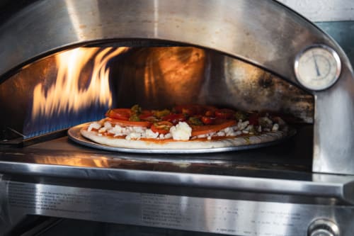 Horno de pizza de leña con pizza fresca cocinándose en Meraki Glampings, Malinalco, México