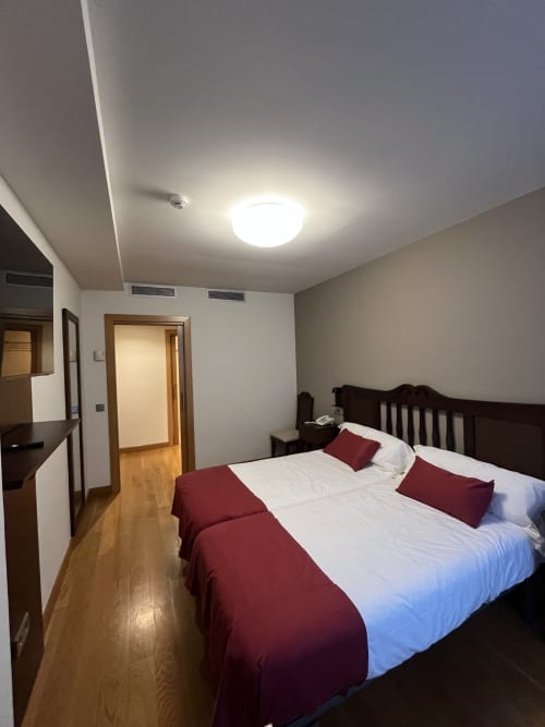 Habitación doble Casa Azcona en Zizur Mayor con camas blancas, almohadas burdeos, suelo de madera y luz de techo