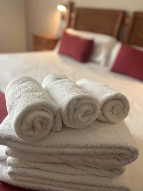 Aufgerollte weiße Handtücher auf dem Bett des Casa Azcona Hotels in Zizur Mayor mit bordeauxroten Kissen und Bergblick
