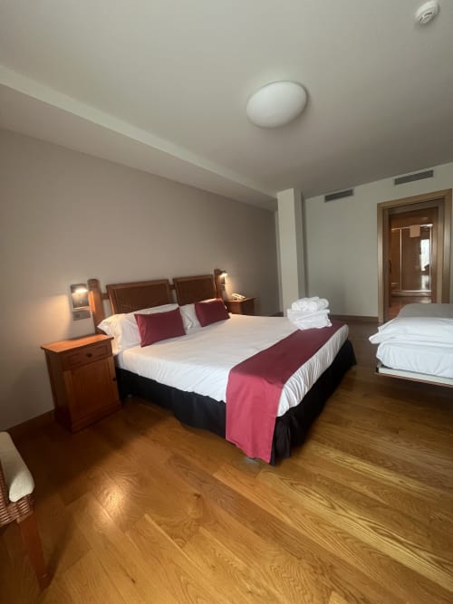 Habitación triple familiar en Casa Azcona en Zizur Mayor con cama de madera, detalles en burdeos y vistas a las montañas