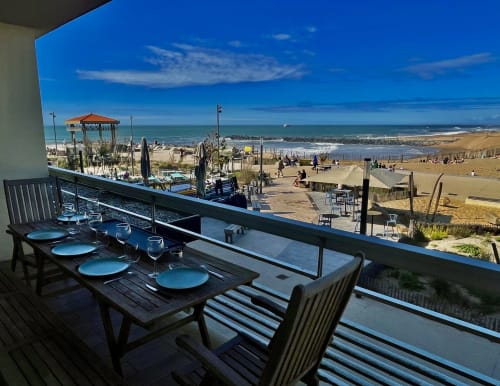 Beachfront terrace dining at Golden Sand Anglet with ocean views, set table, and sandy beach with umbrellas below