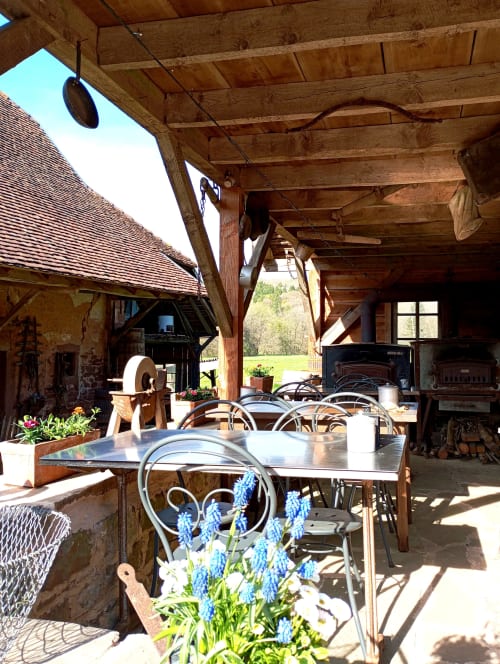 Pergola rustique en bois avec tables métalliques, fleurs bleues et vue sur la campagne à l'auberge Paulusmühle