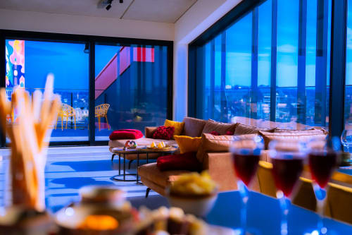 Salon loft luxueux de l'Hôtel Grand Place Mons avec vue sur la ville, canapé moderne et ambiance élégante en soirée