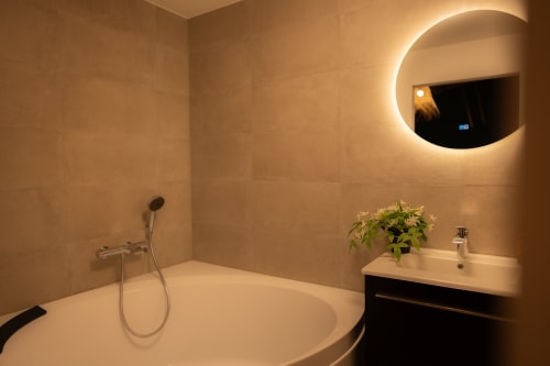 Salle de bains moderne du loft de Mons avec miroir rond lumineux, baignoire, lavabo et douche à effet pluie