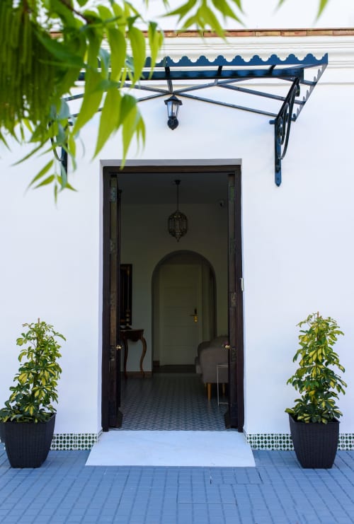 Elegante entrada al Hotel Alcazaba Salobreña con puerta arqueada, pérgola azul, plantas en maceta y patio estilo marroquí
