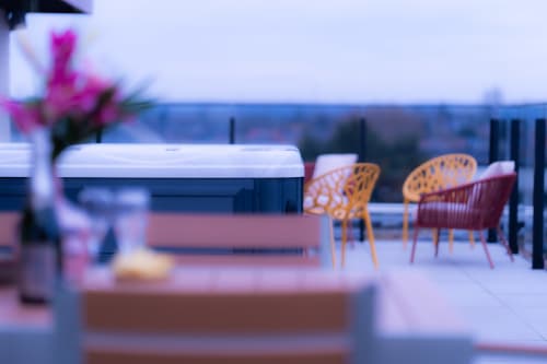 Terrasse panoramique floue de l'Hôtel Grand Place Mons avec chaises orange, fleurs roses et vue sur la skyline