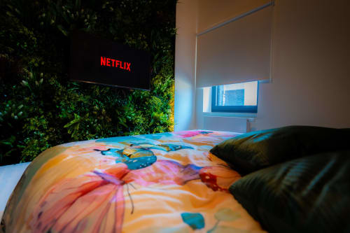 Chambre moderne du Loft de l'Hôtel Grand Place à Mons avec literie colorée, TV écran plat diffusant Netflix et touches de vert