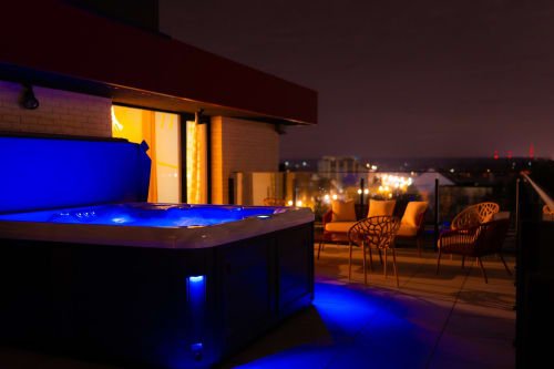 Terrasse panoramique du Hotel Grand Place Loft à Mons avec jacuzzi illuminé, transats et vue sur la ville la nuit