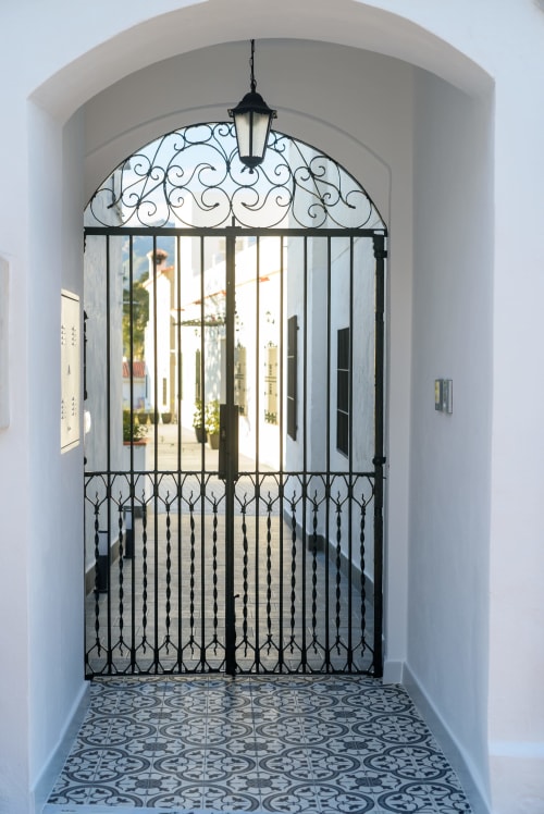 Ornamentada puerta de hierro forjado negro con arco decorativo en entrada de piedra blanca del Hotel Alcazaba Salobreña
