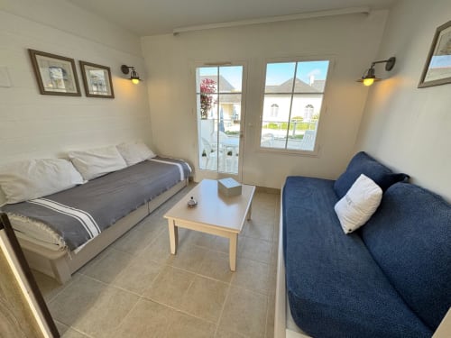Lumineux séjour avec lit, canapé bleu et portes vitrées ouvrant sur balcon avec vue sur Belle-Île-en-Mer, Locmaria