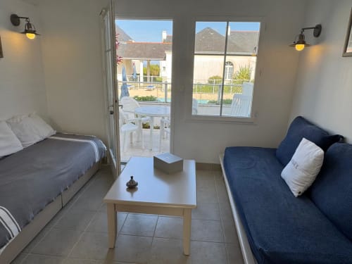 Studio moderne à Locmaria, Belle Île avec lit, canapé bleu, table blanche et terrasse vue piscine et montagnes