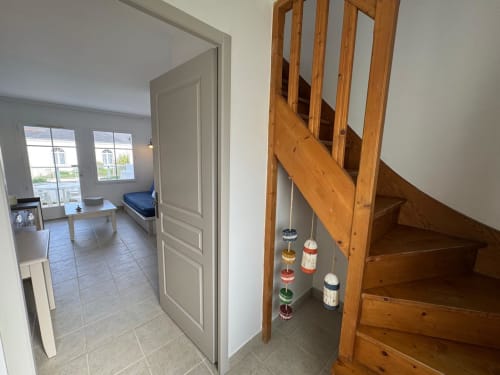 Entrée de l'appartement Belle Île en Mer avec escalier en bois, porte ouverte sur la chambre et décoration côtière.