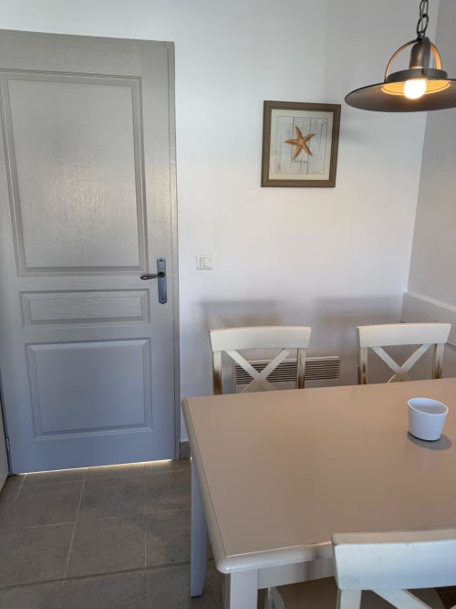 Salle à manger moderne avec chaises X blanches, table en bois et luminaire suspendu aux Locations Loc'Maria, Belle Île en