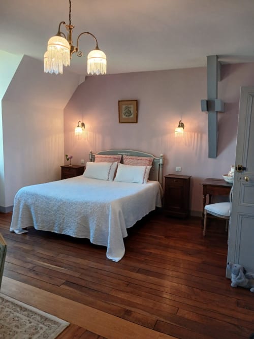 Elegante dormitorio rosa en Château De Clusors con cama blanca, pisos de madera e iluminación vintage de latón