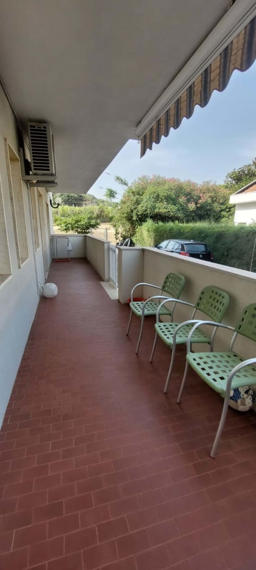 Covered terrace with green chairs and striped awning at Tales of Abruzzo apartment in Casalbordino Lido, overlooking garden