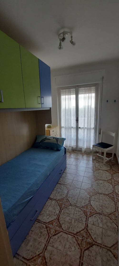 Bright bedroom with blue bed, lime green cabinets, and glass doors at Tales of Abruzzo apartment in Casalbordino.
