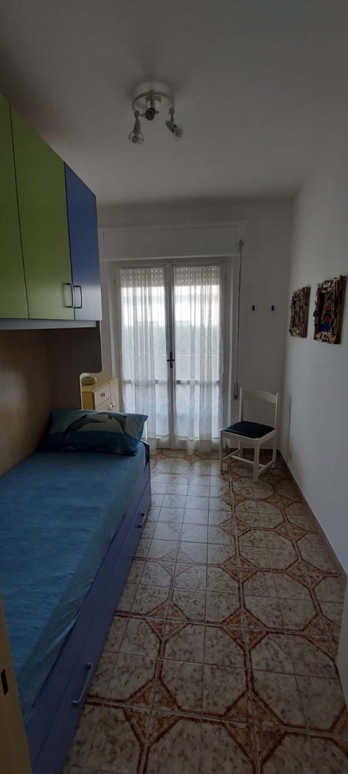 Bright bedroom in Tales of Abruzzo apartment with blue bed, green cabinetry, sea view balcony, tiled floor, ceiling fan