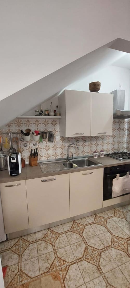 Modern kitchenette with cream cabinetry, patterned backtile, and sloped ceiling in Tales of Abruzzo apartment