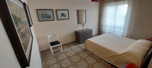 Bright bedroom at Tales of Abruzzo hotel in Atessa with sea view, queen bed, white chair, dark dresser, framed art, and