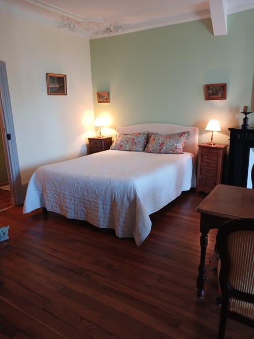 Elegant bedroom at Château De Clusors with queen bed, sage green accent wall, wooden nightstands, and warm lighting in ST