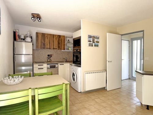 Cuisine-séjour moderne de l'appartement Le Vallon des Sources à Digne-les-Bains, avec appareils inox et table verte.