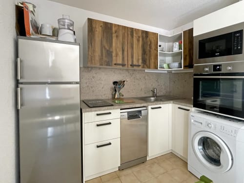 Cuisine moderne de l'appartement Le Vallon des Sources avec appareils en acier inoxydable, armoires crème et machine à laver