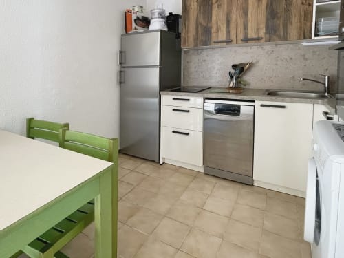 Cuisine moderne avec chaise de salle à manger verte, appareils électroménagers en acier inoxydable et armoires blanches à l'appartement Le Vallon des Sources