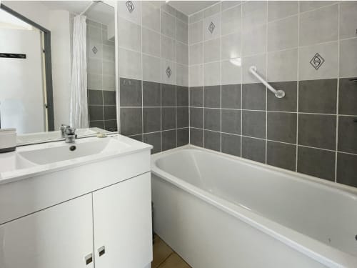 Salle de bain moderne avec lavabo blanc, baignoire, carrelage gris et blanc au Vallon des Sources, Digne-les-Bains