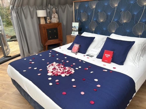 Chambre luxueuse de l'hôtel Bubble Jade avec pétales de roses sur la literie bleu marine, tête de lit élégante et table de nuit en bois à Bazouges