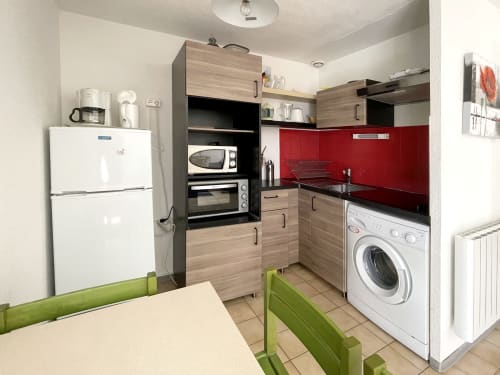 Cuisine moderne avec crédence rouge, meubles en bois, électroménagers blancs et lave-linge au Vallon des Sources