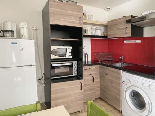 Cuisine moderne avec dosseret rouge, armoires en bois, micro-ondes, four et lave-linge dans un appartement au Vallon des