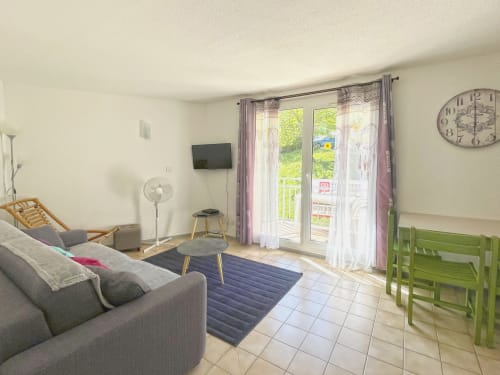 Séjour lumineux de l'Appartement 82 au Vallon des Sources, Digne-les-Bains, avec canapé gris, TV et portes-fenêtres donnant sur la montagne