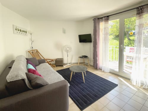 Séjour lumineux à Digne-les-Bains avec canapé gris, TV, portes-fenêtres sur balcon vue montagne, style moderne