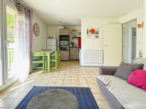 Cuisine ouverte et séjour avec table verte, canapé gris et carrelage en terre cuite à l'Appartement 82 du Vallon des