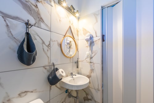 Compact bathroom at Casa de Océano hotel in Tarifa with marble tiles, round mirror, and shower enclosure