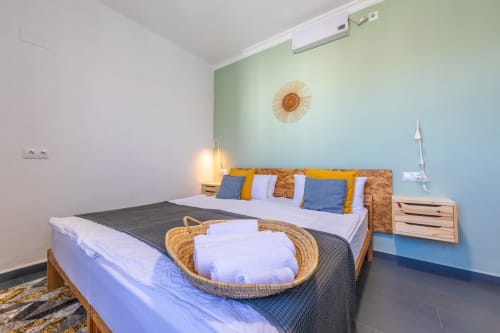 Gregal room at Casa de Océano hotel in Tarifa featuring a wooden bed with colorful pillows, blue accent wall, and modern