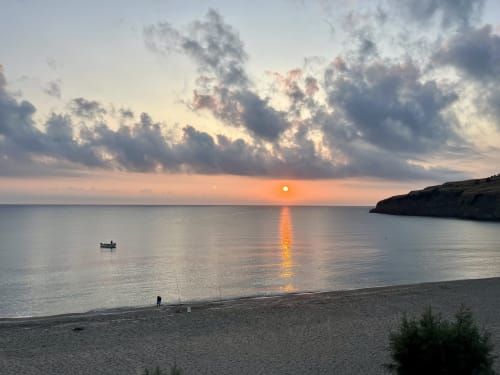 Sunrise over Agnone Bagni beach with fishing boat, golden light reflecting on calm sea waters