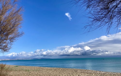 Turquoise sea view from Noemi Holiday House beach in Agnone Bagni with white clouds and sandy shore in the winter season