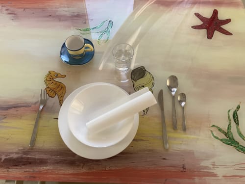 Hand-painted glass on table with coastal-inspired marine motifs, depicting stars, shells, and seahorses, created by Noemi Holiday House.