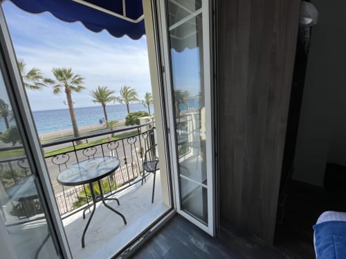 Balcony with sea view at Hotel Flots d'Azur, Nice. Elegant outdoor seating overlooking Mediterranean Sea and palm trees.