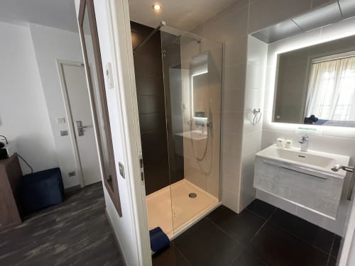 Modern bathroom at Hotel Flots d'Azur in Nice with glass shower, white sink, and heated mirror
