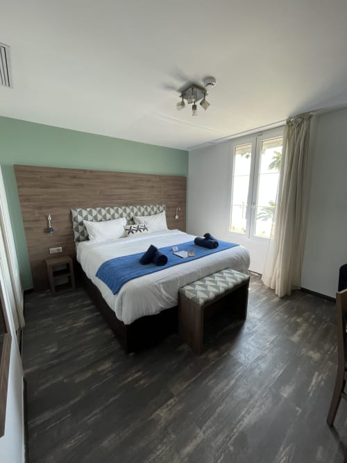 Chambre moderne à l'Hôtel Flots d'Azur à Nice avec mur d'accent vert menthe, tête de lit en bois, vue mer et style contemporain