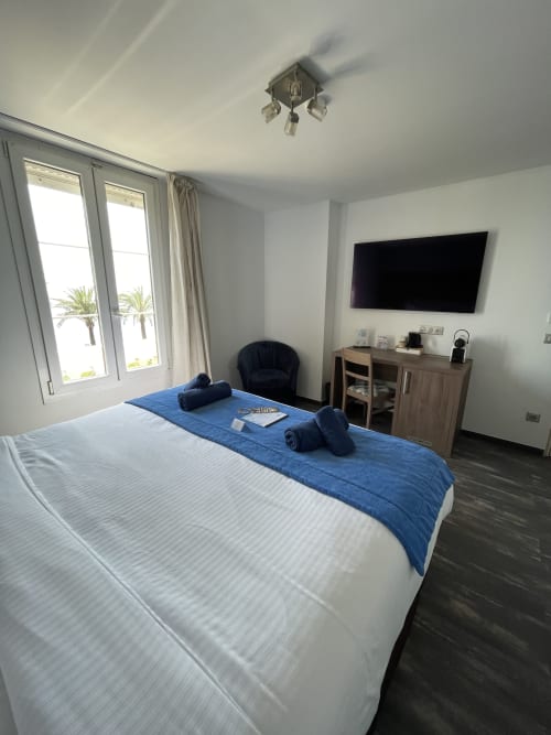 Chambre d'hôtel moderne et lumineuse avec vue mer, lit double, TV, bureau et baies vitrées panoramiques à l'Hôtel Flots d'Azur à Nice