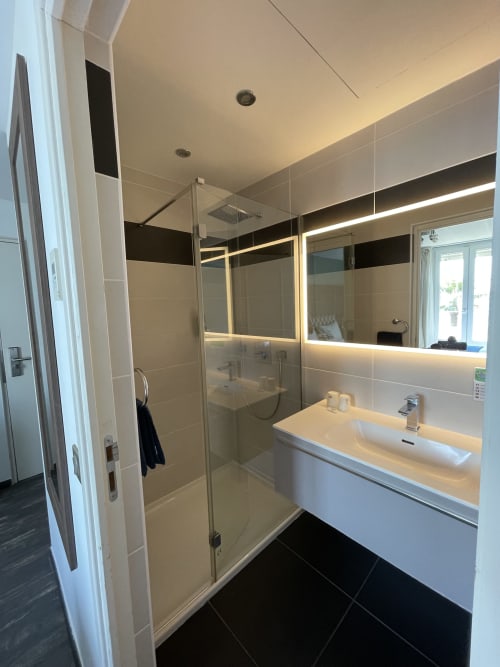 Salle de bain moderne de l'Hôtel Flots d'Azur à Nice avec douche à l'italienne, miroir lumineux et vasque blanche