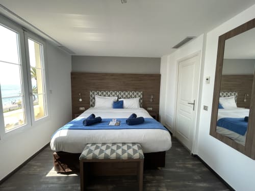 Modern hotel bedroom at Hotel Flots d'Azur Nice with sea view, king bed, dark wood headboard, and contemporary furnishings.